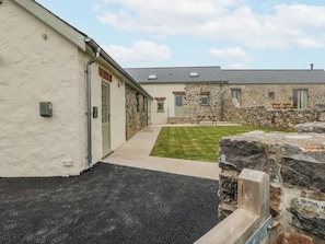 A building with a stone facade, a paved walkway, and a grassy area with a picnic table. - Barley Cottage (Swansea)