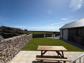 Un mur de pierre, une pelouse verdoyante et une table de pique-nique en bois dans une cour offrant une vue sur l’horizon.