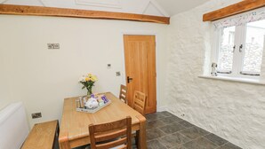 A room with a wooden dining table, chairs, a bench, a door, a window, and a radiator. - Barley Cottage (Swansea)