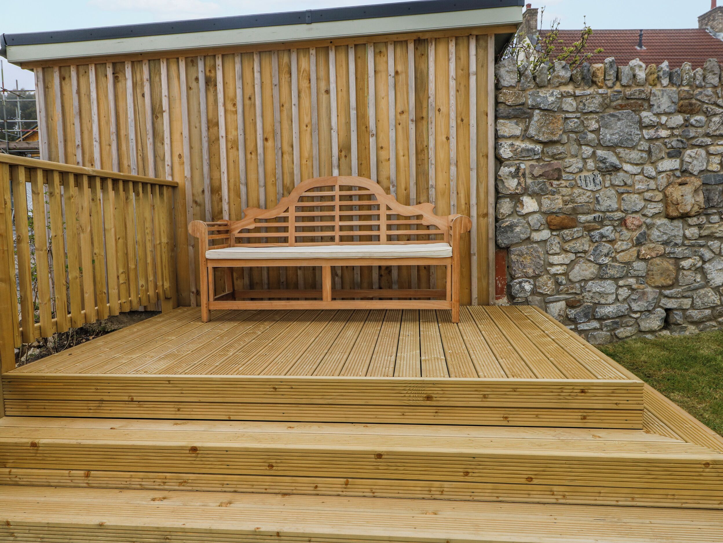 Eine Holzterrasse mit einer Bank, einer Steinmauer und einem Holzzaun.