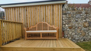 A wooden deck with a bench, a stone wall, and a wooden fence. - Barley Cottage (Swansea)
