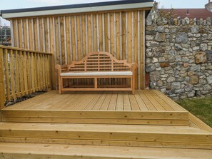 A wooden deck with a bench, a stone wall, and a wooden fence. - Barley Cottage (Swansea)