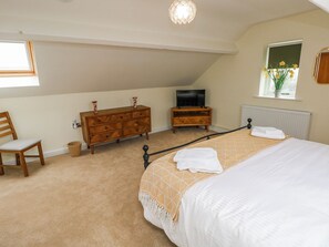 A bedroom with a bed, a wooden dresser, a television, a window with flowers, and a chair. - Barley Cottage (Swansea)