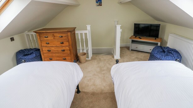 A bedroom with two beds, a dresser, a television, and a small picture on the wall. - Barley Cottage (Swansea)