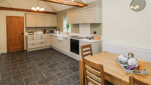 A kitchen with wooden beams, a skylight, a clock, and a dining area with a tray of items. - Barley Cottage (Swansea)