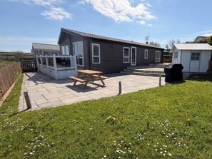 A house with a patio, a wooden table, and a small garden. - Wernlas Lodge (Swansea)
