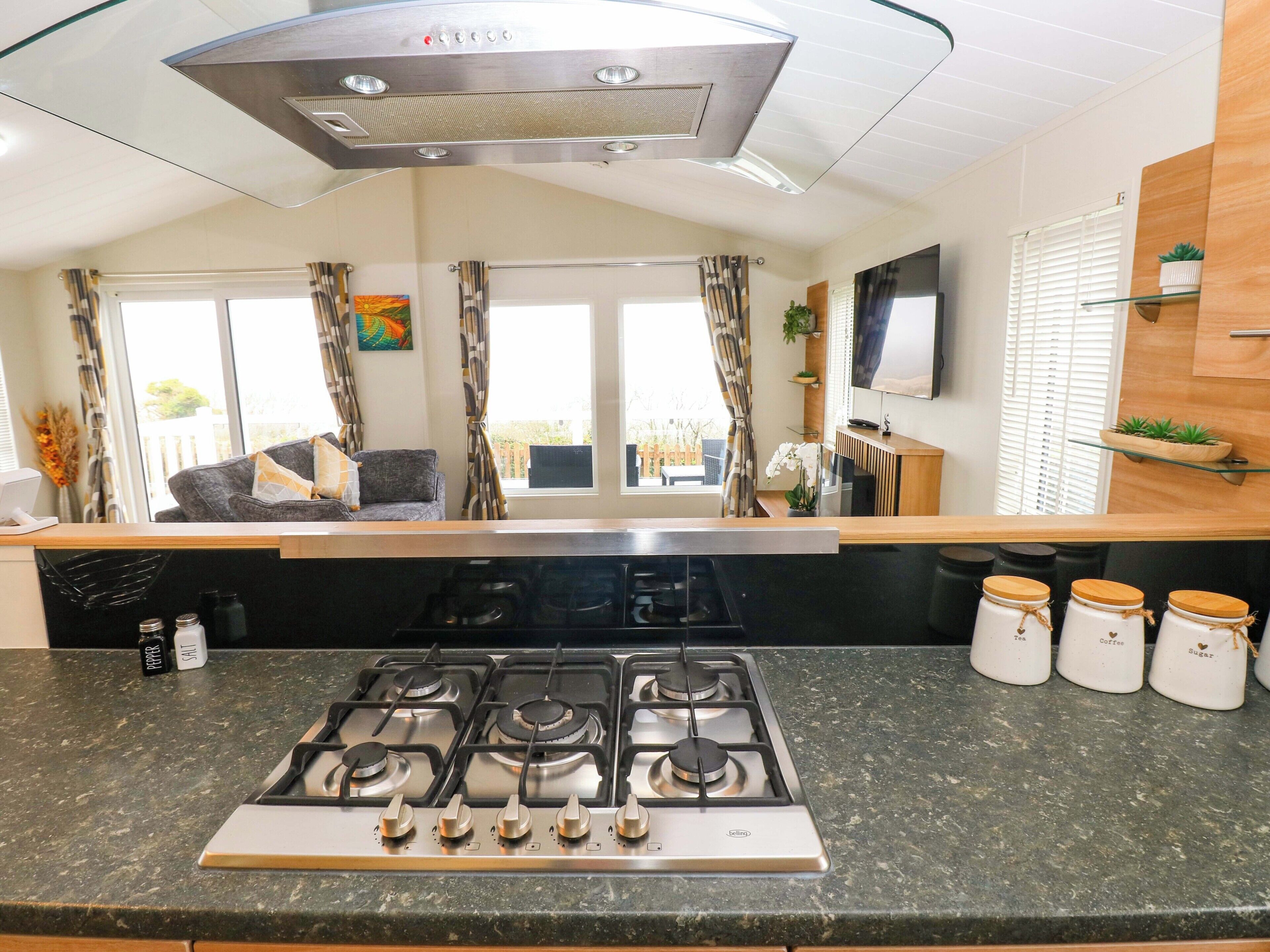 A modern kitchen with a gas stove, a flat-screen TV, and a window with curtains.