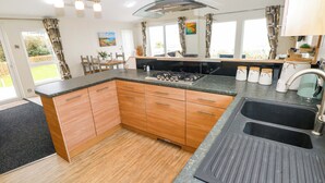 A modern kitchen with wooden cabinets, a gas stove, and a large sink. - Wernlas Lodge (Swansea)