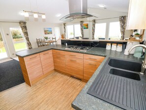 A modern kitchen with wooden cabinets, a gas stove, and a large sink. - Wernlas Lodge (Swansea)