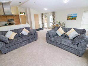 A living room with two grey sofas, a kitchen area, and a dining table with chairs. - Wernlas Lodge (Swansea)