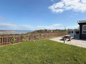 A grassy outdoor area with a wooden fence, a picnic table, and a building with a tiled roof. - Wernlas Lodge (Swansea)