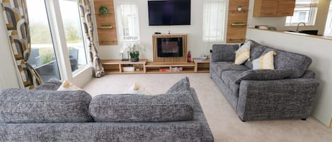 A living room with grey sofas, a flat-screen TV, wooden cabinets, and a window with curtains.