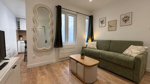 A modern living room with a green sofa, a wooden coffee table, a large mirror, and a kitchen in the background. - Modern, Renovated Studio in the Heart of La Rochelle by Kaz'Concept (La Rochelle)