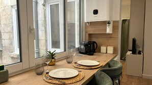 A dining area with a wooden table set for two, a coffee maker, and a refrigerator. - Modern, Renovated Studio in the Heart of La Rochelle by Kaz'Concept (La Rochelle)