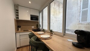 A modern kitchen with a wooden countertop, two bar stools, a coffee machine, and a view of the street through large windows. - Modern, Renovated Studio in the Heart of La Rochelle by Kaz'Concept (La Rochelle)