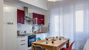 Une cuisine moderne avec des meubles blancs, une table à manger en bois et une chaise rouge.