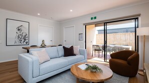 A modern living room with a light blue sofa, a brown armchair, a round wooden coffee table, and a framed artwork on the wall.