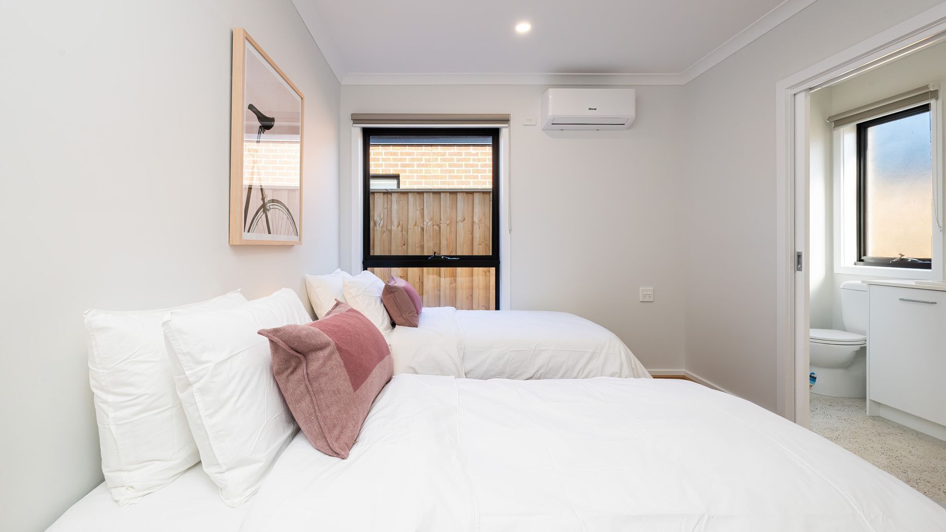 Ein Schlafzimmer mit zwei Betten, einem Fenster, einer Klimaanlage und einer Tür zu einem Badezimmer.