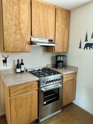 A kitchen with wooden cabinets, a stainless steel gas stove, an oven, and a coffee maker.