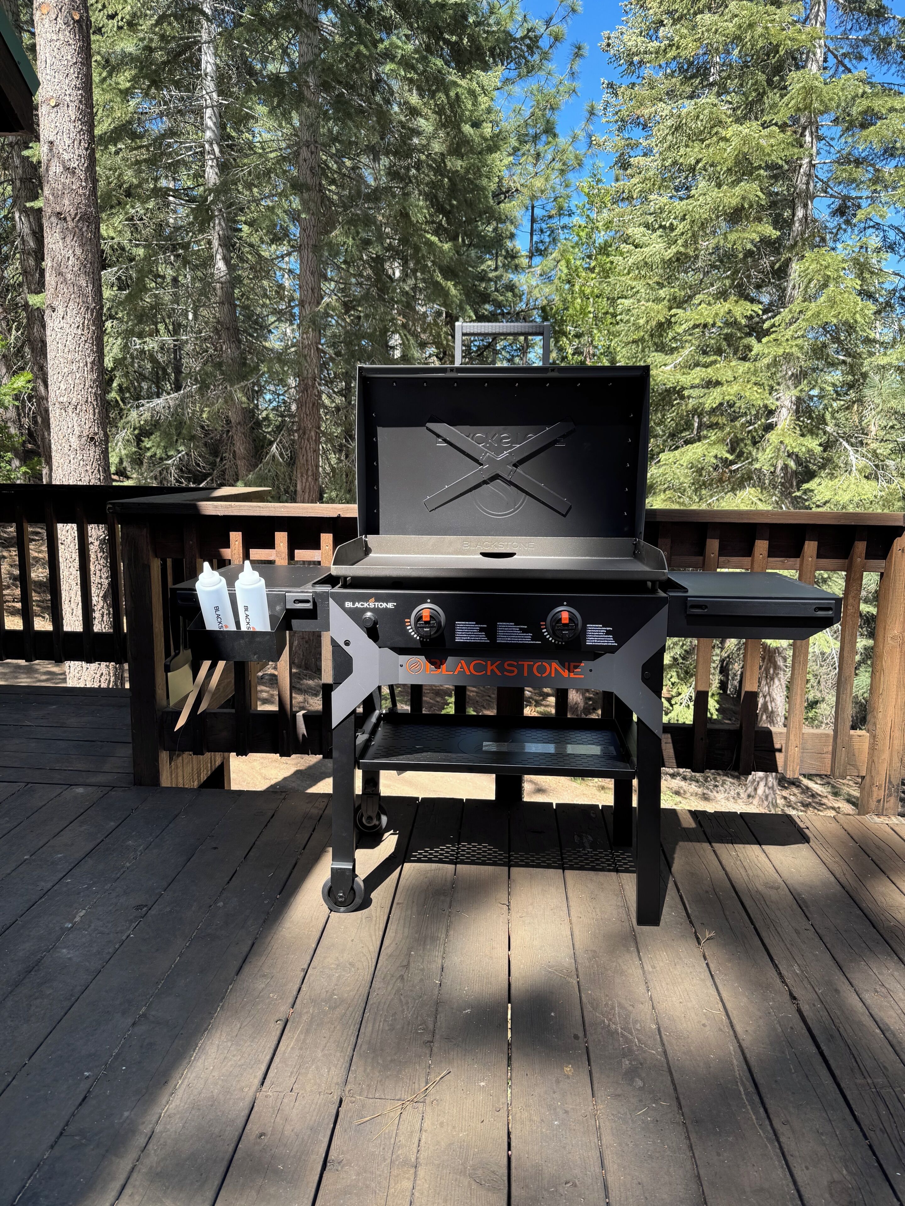Un barbecue Blackstone sur une terrasse en bois, avec vue sur les arbres.