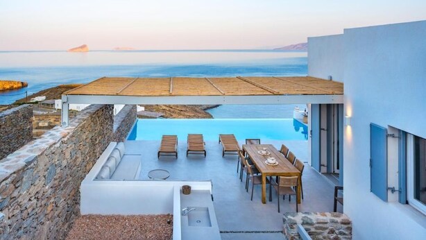 A modern outdoor pool area with a view of the sea, a wooden deck, and a dining table with chairs. - MZ Deep Blue (Kithnos)