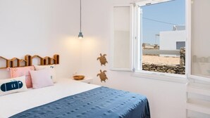 A bedroom with a bed, a window with a view, a wooden headboard, and wall decor. - MZ Deep Blue (Kithnos)
