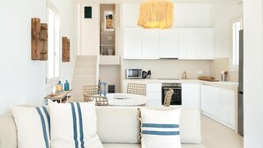 A modern kitchen with white cabinets, a dining area with a round table, and a sofa with striped cushions. - MZ Deep Blue (Kithnos)