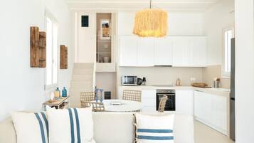 A modern kitchen with white cabinets, a dining area with a round table, and a sofa with striped cushions.