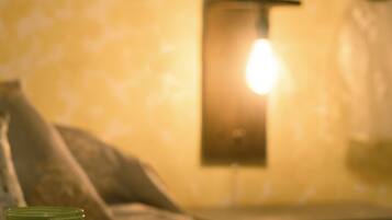 Un lit avec un livre et une bougie, une lampe fixée au mur et un mur décoré d’un motif.