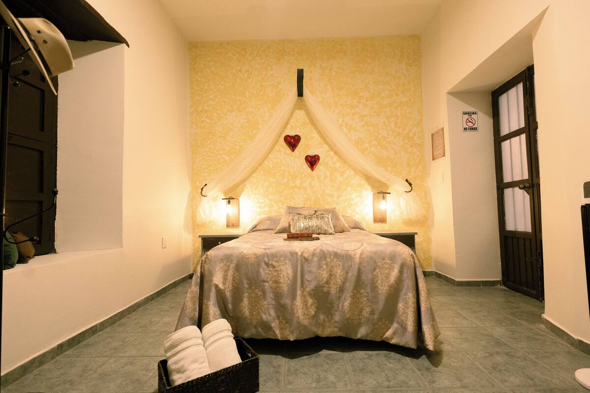 A hotel room with a bed, two bedside lamps, a wall-mounted clock, and a door with a window.