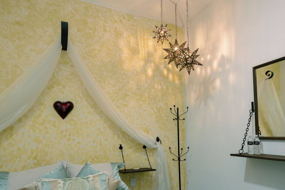 A bedroom with a bed, a heart-shaped decoration, a star-shaped hanging light, and a mirror on the wall.