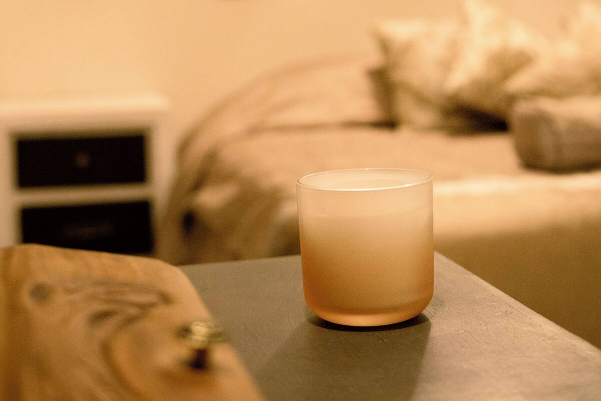 A candle on a table in a dimly lit room with a bed and a wall decoration in the background.