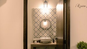 Un baño con puerta de madera, un lavabo con espejo, papel tapiz estampado y una planta pequeña sobre el mostrador.
