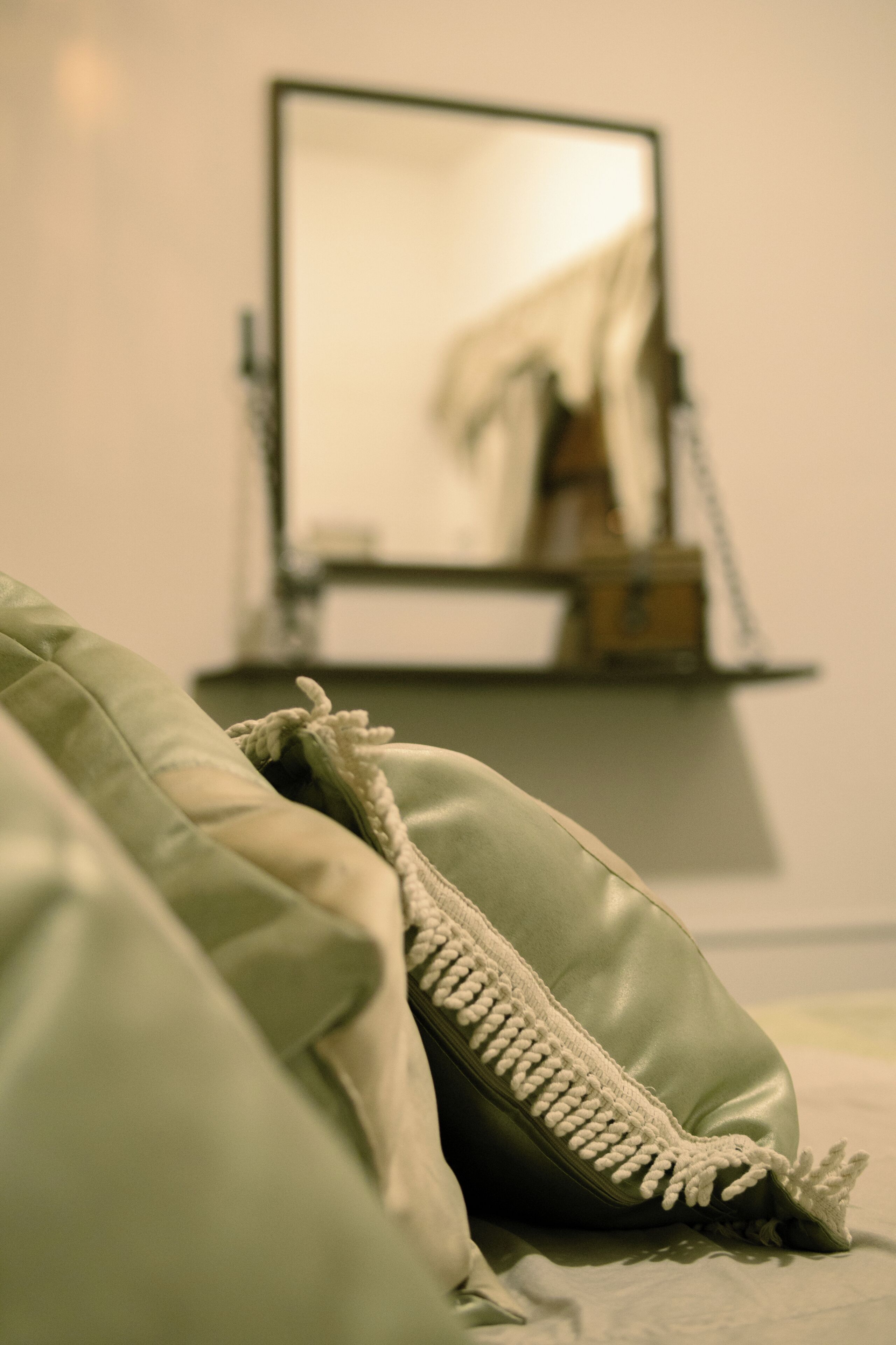 A bed with a green blanket and a pillow with a tassel detail.