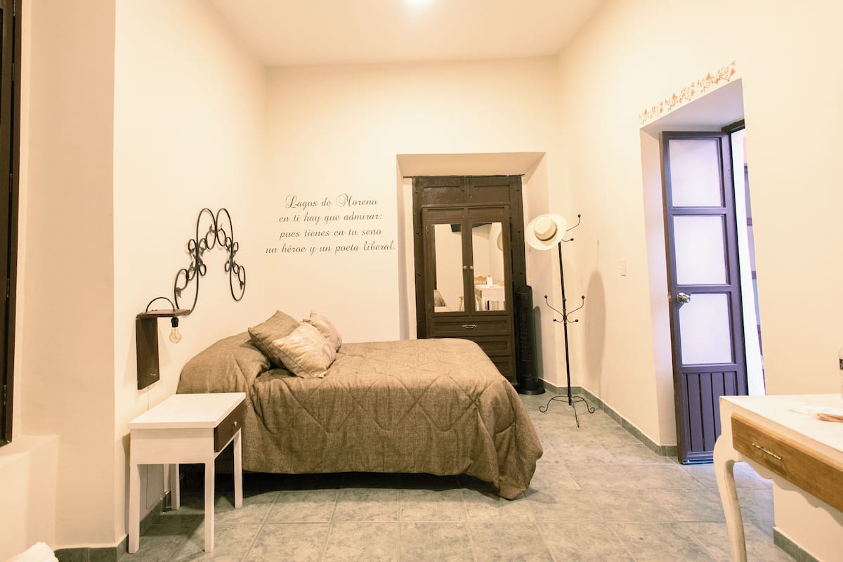 A bedroom with a bed, bedside table, and a wall with a decorative light fixture.