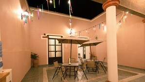Un patio al aire libre con mesas y sillas, luces colgantes y una planta en maceta.