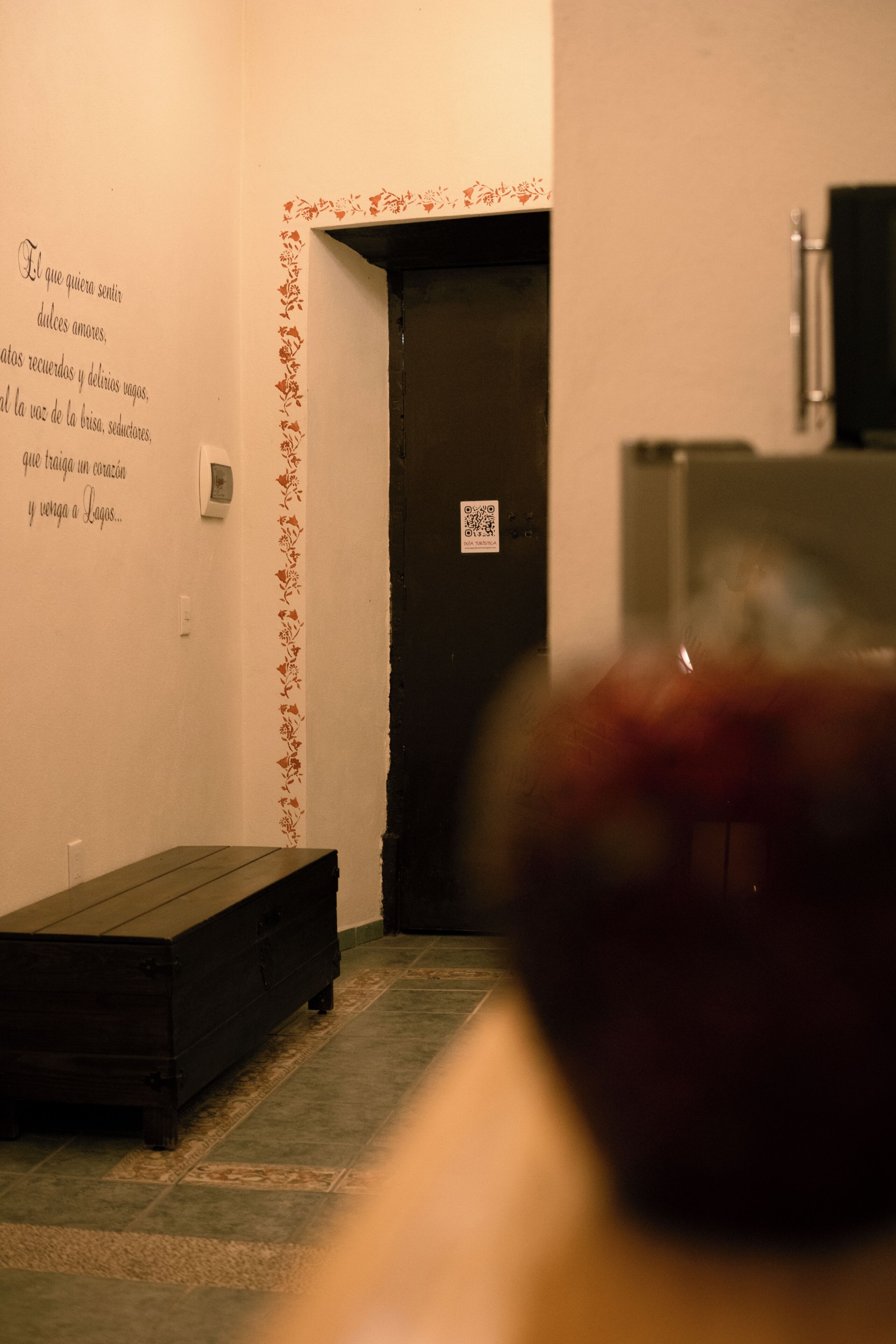 A room with a wooden bench, a door, and a wall with a floral border.