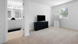 Een kamer met een witte badkamer, een zwarte entertainmentsunit en een raam met zonwering.