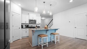Een moderne keuken met witte kasten, een centraal eiland met krukken, een magnetron en een koffieapparaat.