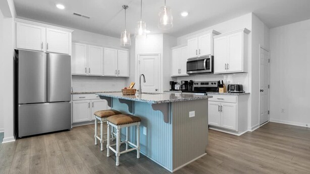 Een moderne keuken met witte kasten, roestvrijstalen apparatuur, een blauw kookeiland met krukken en hanglampen.