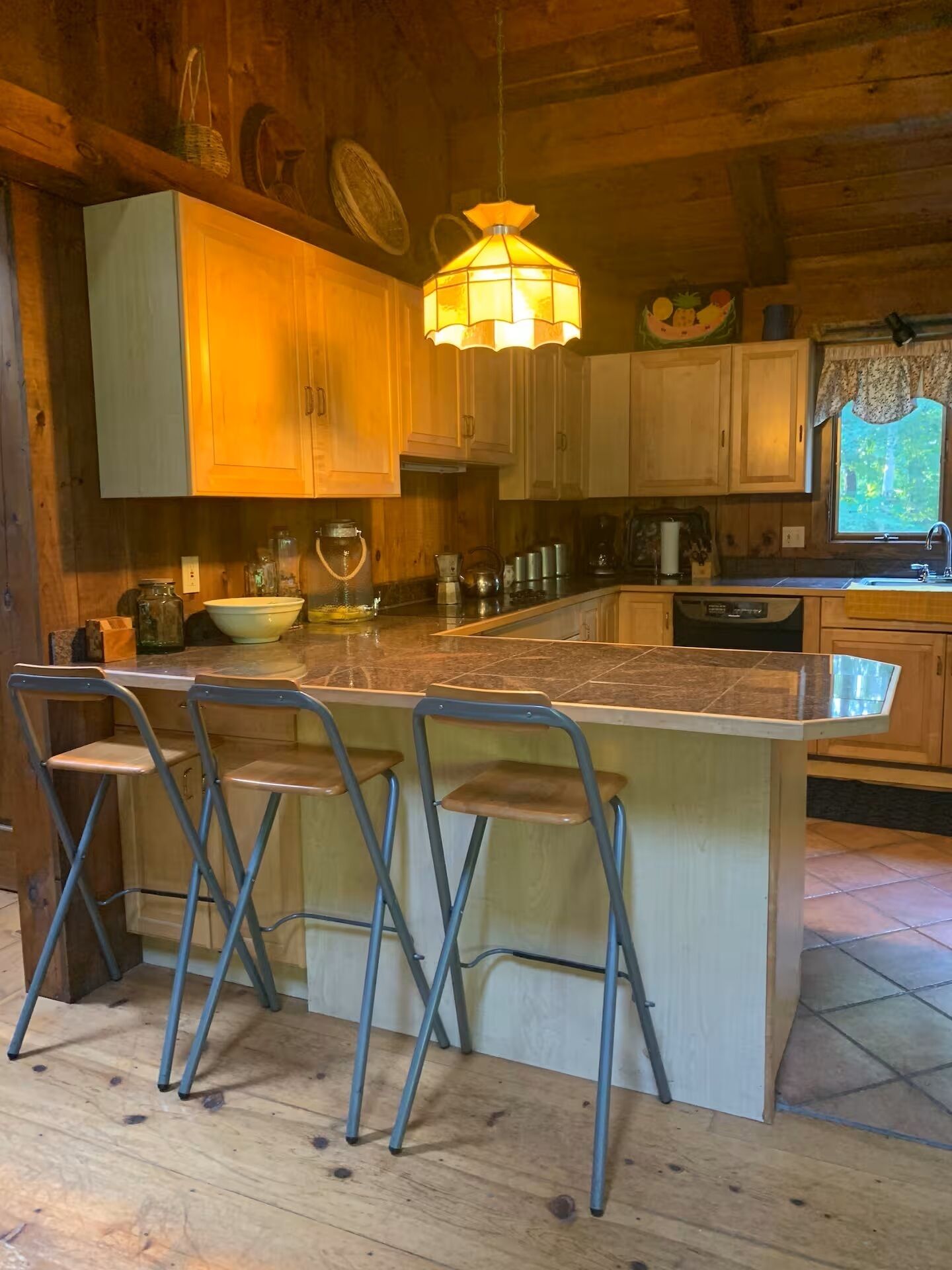 Interieur van een houten blokhut met een keuken, inclusief een groot kookeiland, barstoelen en een hanglamp.