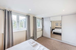 Ein Schlafzimmer mit einem Bett, einem großen Spiegel und Blick auf einen Garten durch das Fenster.