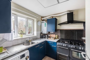 Eine kleine Küche mit Herd, Backofen und Spüle, ausgestattet mit blauen Schränken und einem Fenster mit Blick.