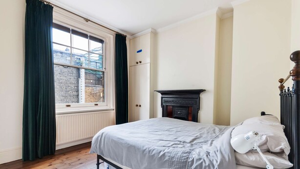 A bedroom with a bed, a radiator, a window with curtains, a dresser, and a lamp. - Chic Spacious Holborn Apartment (London)