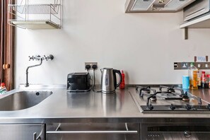 Eine Küche mit Spülbecken aus Edelstahl, Toaster, Wasserkocher, Gasherd und verschiedenen Küchenutensilien auf der Arbeitsfläche.