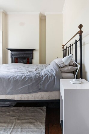 A neatly made bed with a headboard, a bedside lamp, and a small white nightstand. - Chic Spacious Holborn Apartment (London)