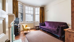 A room with a purple sofa, a yellow chair, a small table, and a TV on a stand. - Chic Spacious Holborn Apartment (London)