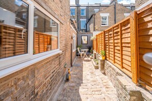 A narrow brick alleyway with a wooden fence, a small table with chairs, and a potted plant. - Rare 5 bed House in Vauxhall With Roof Terrace (London)