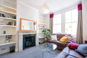 A living room with a fireplace, bookshelves, a sofa, and a glass coffee table. - Rare 5 bed House in Vauxhall With Roof Terrace (London)