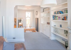Ein modernes Wohnzimmer mit Essbereich, weißen Wänden, einer Bücherwand und einem großen Fenster.